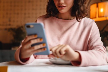 Kahve içerken cep telefonuyla kahve içen güzel esmer bir kadının kesilmiş fotoğrafı..