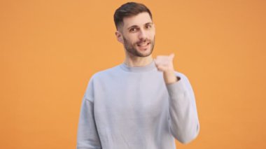 Genç, mutlu, iyimser adam sarı duvar arkaplanından izole edilmiş ve baş parmağını kaldırmış.