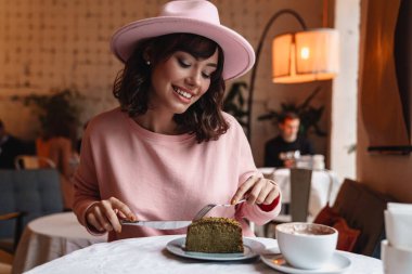 Güzel, esmer, neşeli, pozitif bir kadının kafede çekilmiş fotoğrafı. Pasta yiyor, kahvaltı yapıyor..