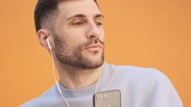 Genç mutlu adam, sarı duvar arkasında izole edilmiş. Kulaklıkla müzik dinliyormuş.