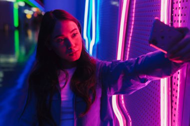 Neon bir duvarın önünde duran uzun siyah saçlı güzel Asyalı kadın.