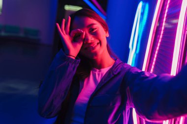 Neon bir duvarın önünde duran uzun siyah saçlı güzel Asyalı kadın.
