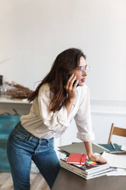 Güzel, genç, esmer bir kadın kafede çalışırken cep telefonuyla konuşuyor, masada duruyor.