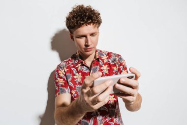 Beyaz arka planda izole edilmiş cep telefonuyla video oyunu oynayan genç adam görüntüsü