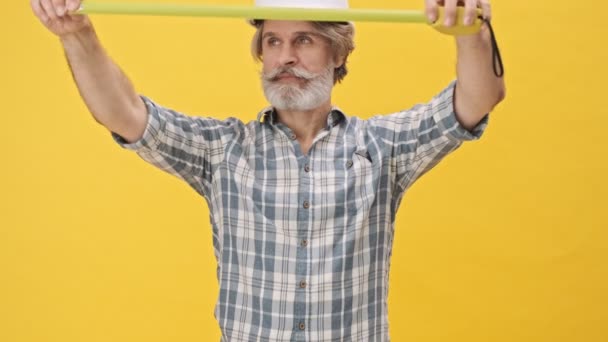 Senior Optimistische Man Bouwer Helm Geïsoleerd Gele Achtergrond Holding Centimeter — Stockvideo