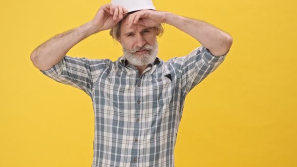 Sénior Homem Cansado Construtor Capacete Isolado Sobre Fundo Amarelo — Vídeo de Stock