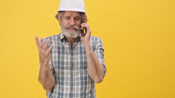 Verward Man Bouwer Helm Geïsoleerd Gele Achtergrond Praten Door Mobiele — Stockvideo