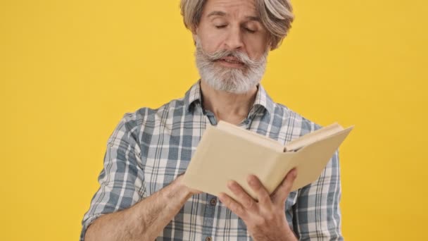 Hombre Concentrado Mayor Aislado Sobre Fondo Amarillo Libro Lectura Saludando — Vídeo de stock