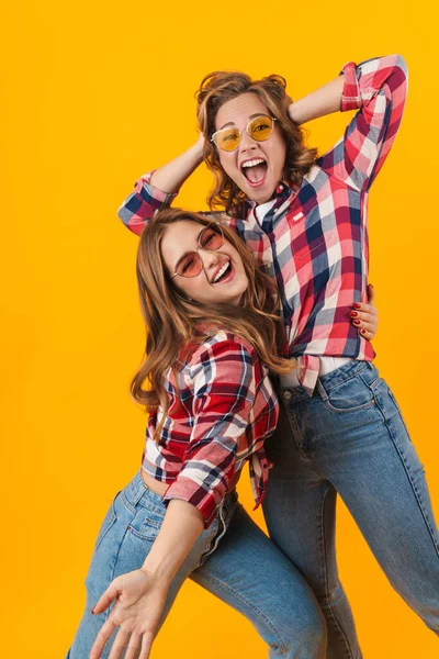 两个年轻漂亮的女孩穿着格子花衬衫 在黄色的背景上享受着孤独的乐趣 — 图库照片