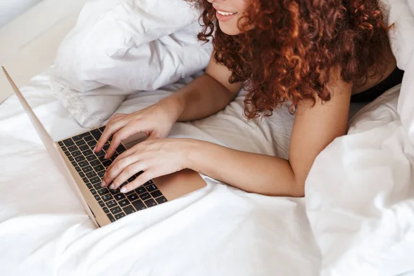 在家里的旅馆里 一位红头发的年轻女士穿着内衣裤躺在舒适的床上 她的照片是用笔记本电脑剪下来的 — 图库照片