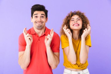 Kafkasyalı kadın ve erkeğin portresi. Parmaklarını çapraz tutuyor ve mor arka planda izole edilmiş iyi şanslar diliyor.