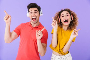 Genç beyaz kadın ve erkeğin portresi, müzik dinlerken gülümseyen adam ve kadının, menekşe arka planında izole edilmiş kulaklıklarla.