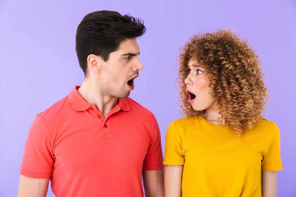 強調された若いカップルの男性と女性の肖像画は 紫色の背景に隔離されたお互いを見ながら 開いた口で怒りを表現します — ストック写真