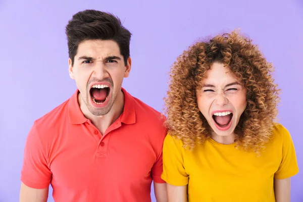 感情的な若いカップルの男性と女性の肖像画の基本的なTシャツ一緒に叫んでカメラで隔離された紫色の背景 — ストック写真