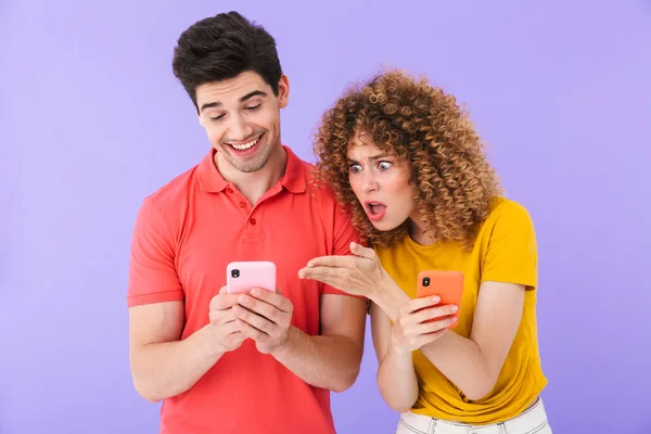 基本的な服を着た白人夫婦の男性と女性の肖像 紫色の背景に隔離された男性のスマートフォンで眉をひそめ 見ている女性 — ストック写真