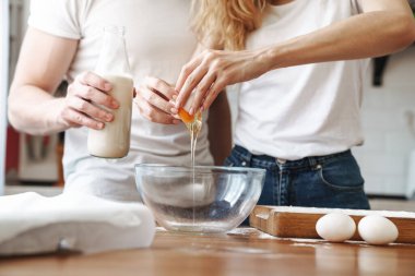 Evde süt ve yumurtalarla kahvaltı hazırlayan genç bir çiftin kırpılmış görüntüsü.