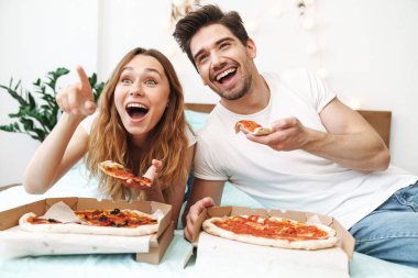 Mutlu bir çiftin evde yatıp pizza yediği görüntüsü.