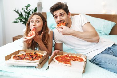 Mutlu bir çiftin evde yatıp pizza yediği görüntüsü.