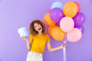 Çok renkli hava balonları ve menekşe arka planda izole edilmiş hediye kutusuyla doğum gününü kutlayan güzel bir genç kadın resmi