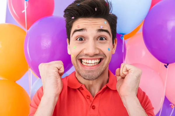 图片特写的是一个快乐的黑发男人 他的脸上挂着闪闪发光的星星 在紫色的背景上孤立着五彩斑斓的气球 高兴极了 — 图库照片