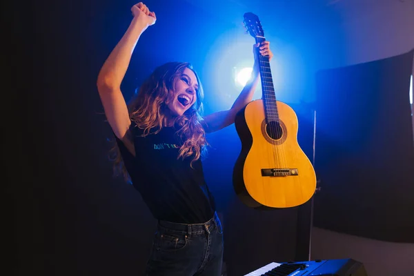 感情的な美しい若い女性音楽家のイメージは フラッシュライトで暗い背景の上にナイトクラブでシーンのギターで再生します — ストック写真