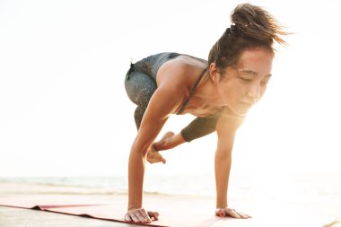 Eşofmanlı spor kadının sabah deniz kenarında yoga yaparken çekilmiş fotoğrafı.