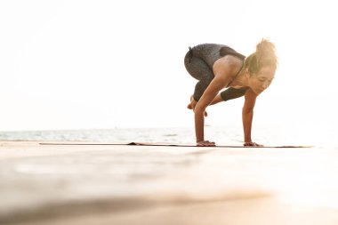 Eşofmanlı güzel sporcu kadının sabah deniz kenarında yoga yaparken çekilmiş fotoğrafı.