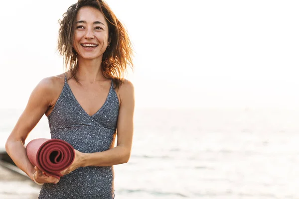 Photo Brunette Sportswoman Tracksuit Smiling Standing Yoga Mat Seaside Morning — Stock Photo, Image