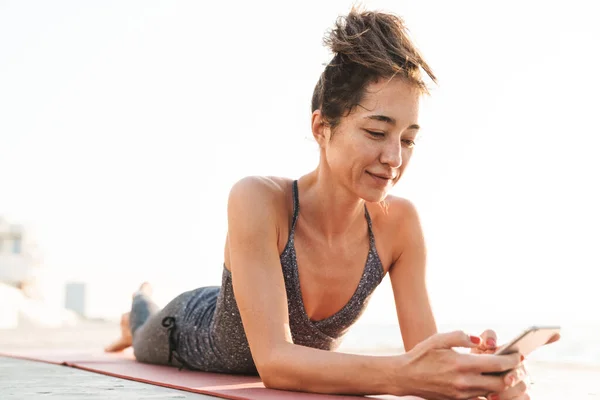 Foto Una Deportista Morena Chándal Sosteniendo Smartphone Tumbada Una Colchoneta — Foto de Stock