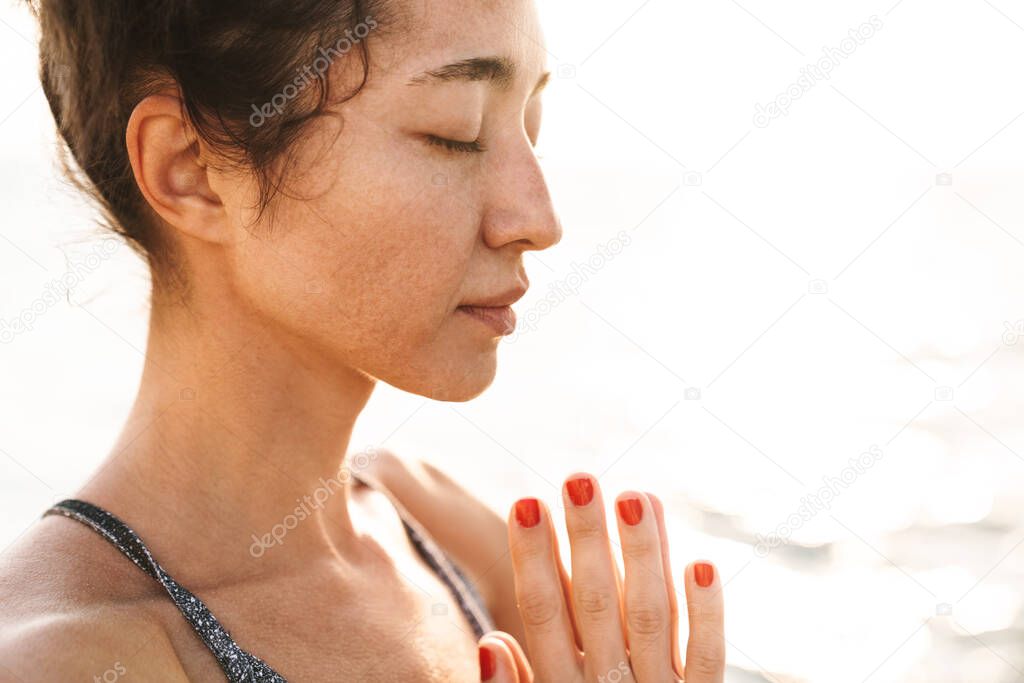 Photo of caucasian fitness woman in tracksuit meditating and keeping palms together while practicing yoga in morning outdoors