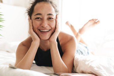 Evde, evde, yatakta gülümseyen neşeli genç bir kadının görüntüsü..