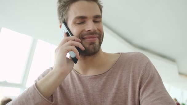 室内のカフェに座っている間 誰かと電話で話している若い髭の男 — ストック動画