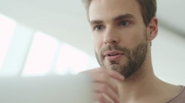 Kafede otururken bilgisayarına bakan odaklanmış sakallı genç bir adamın yakın plan görüntüsü.