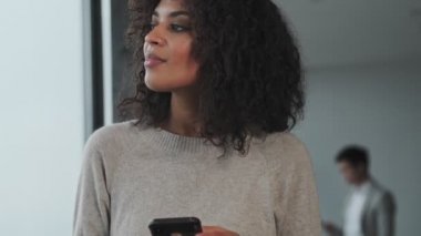 Ofiste cep telefonu kullanan inanılmaz iyimser Afrikalı genç iş kadını.