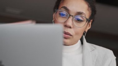 İnanılmaz konsantre olmuş Afrikalı genç iş kadını ofiste dizüstü bilgisayar kullanıyor.