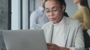 Ofiste dizüstü bilgisayar ve cep telefonu kullanan Afro-Afrikalı genç iş kadını.