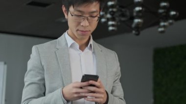 Ofisteki yakışıklı Asyalı genç iş adamı cep telefonu kullanıyor.
