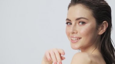 Baştan çıkarıcı, yarı çıplak, ıslak saçlı bir kadının yan görüntüsü kameraya dönüyor ve stüdyoda açık mavi bir arkaplanda izole bir şekilde poz veriyor.