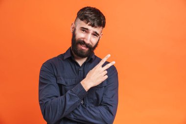 Burun mücevherleri takan, siyah gömlekli, gülümseyen ve turuncu arka planda izole edilmiş barış işareti gösteren mutlu bir adam resmi.