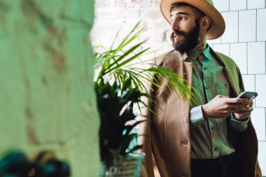 Çekici, sakallı bir adam. Kapalı bir kafede otururken cep telefonu kullanıyor.