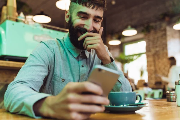 Привабливий Усміхнений Молодий Бородатий Чоловік Сорочці Використовуючи Мобільний Телефон Сидячи — стокове фото