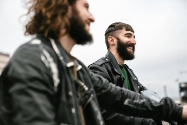 Deri ceketli, sakallı, neşeli adamların fotoğrafı. Dışarıda dururken gülümseyen ve konuşan motosikletliler.