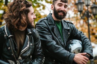 Güz sokağında dikilirken gülümseyen ve konuşan yakışıklı, neşeli adamların fotoğrafı.