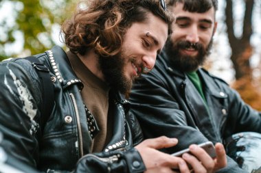Güz sokağında dururken gülümseyen ve cep telefonu kullanan yakışıklı, neşeli adamların fotoğrafı.