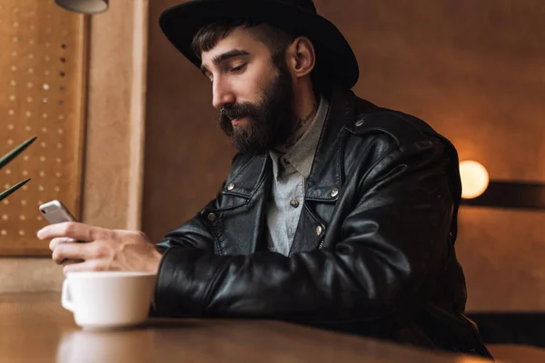 Photo Handsome Young Man Wearing Hat Using Smartphone While Drinking — Stock Photo, Image