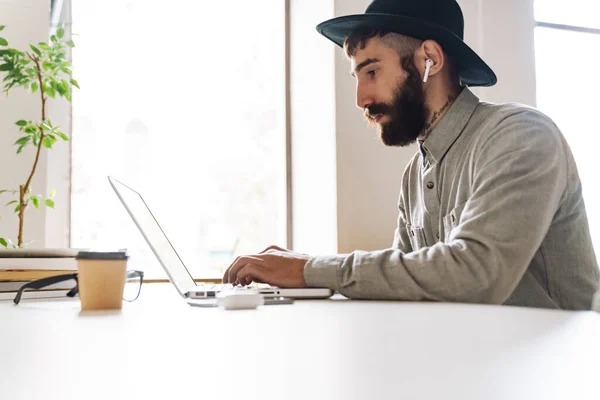 Ofisteki Masada Otururken Dizüstü Bilgisayar Kulaklık Kullanan Ciddi Bir Genç — Stok fotoğraf