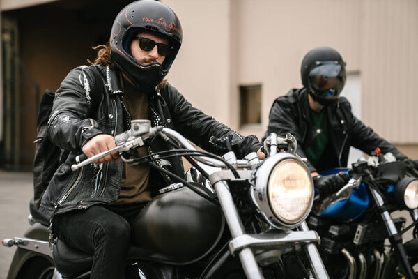 Photo of bearded brutal men bikers on bikes wearing helmets looking at camera outdoors