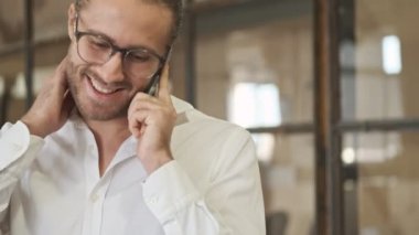 Yakışıklı, mutlu, pozitif iş adamı ofiste cep telefonuyla konuşuyor.