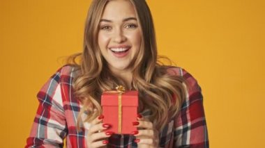Sarı arka planda izole edilmiş genç mutlu pozitif kız size bir hediye kutusu verir.