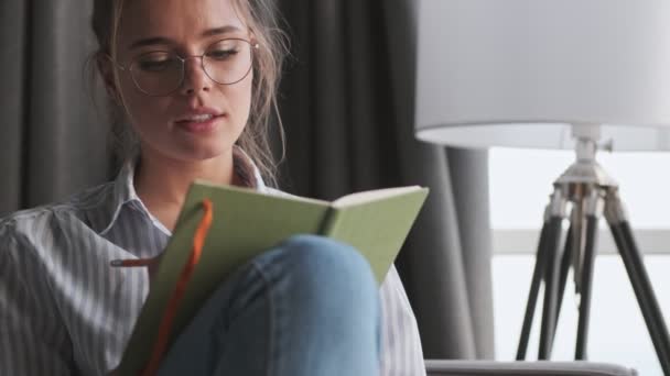 Uma Jovem Calma Usando Óculos Está Contorcendo Seu Caderno Sentado — Vídeo de Stock